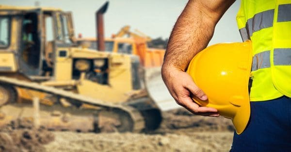 blog picture of construction site background worker's hand holding his hard hat