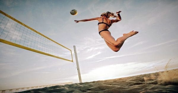 blog picture of a lady playing beach volleyball jumping high for a spike