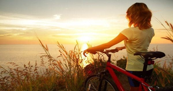 blog picture of a lady walking her bicycle by the ocean during sunset