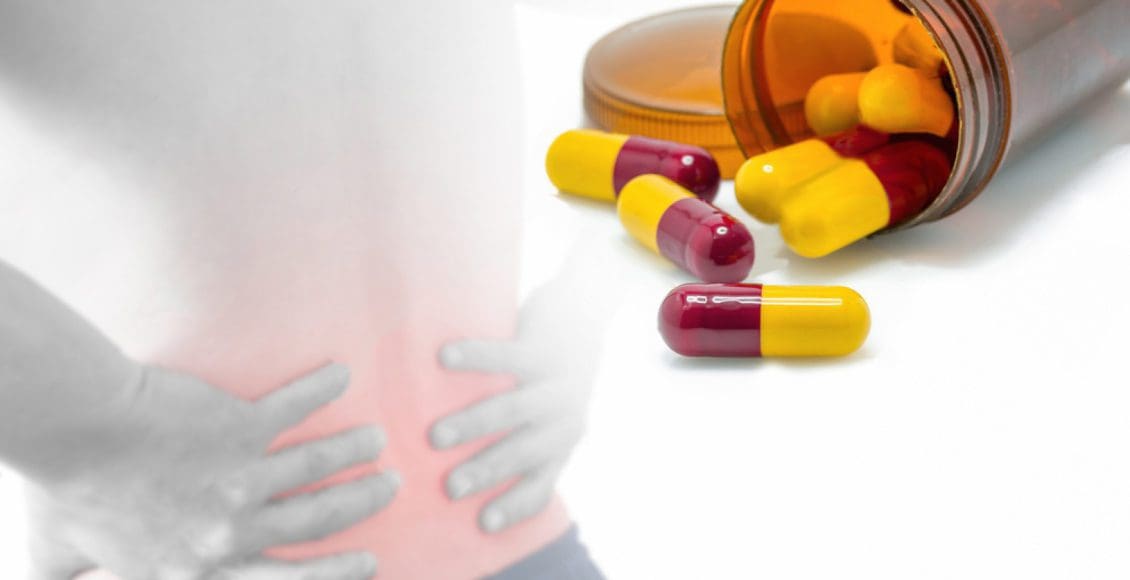 man grabbing lower back in pain and a bottle of pain medication open with capsules out of bottle