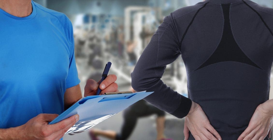 chiropractor takes notes on lady with back pain in gym